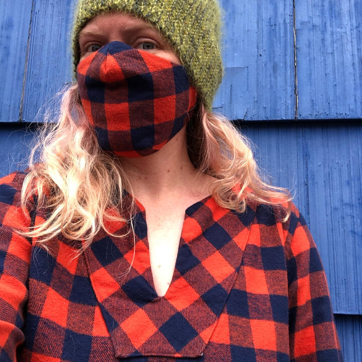 Lee wearing red/orange plaid flannel top with slit neck and matching flannel mask, and a fuzzy green hat